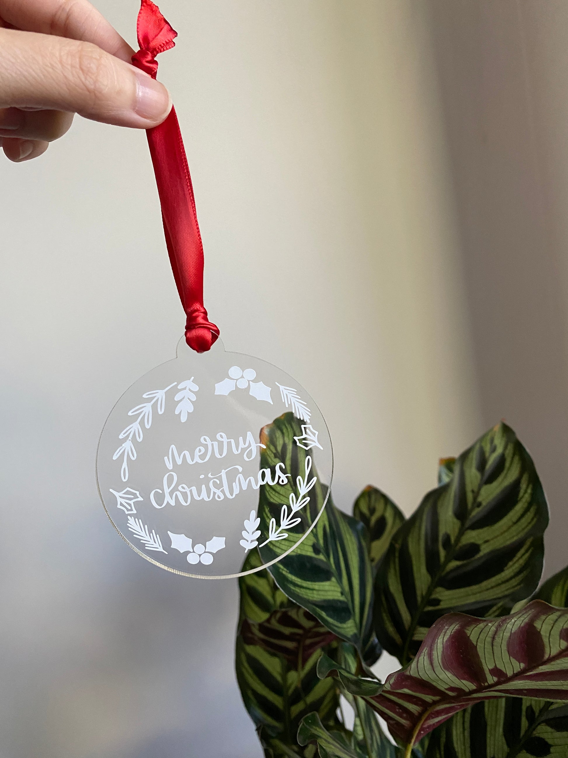 Clear acrylic Christmas ornament displaying 'merry christmas' surrounded by a design of leaves and holly.